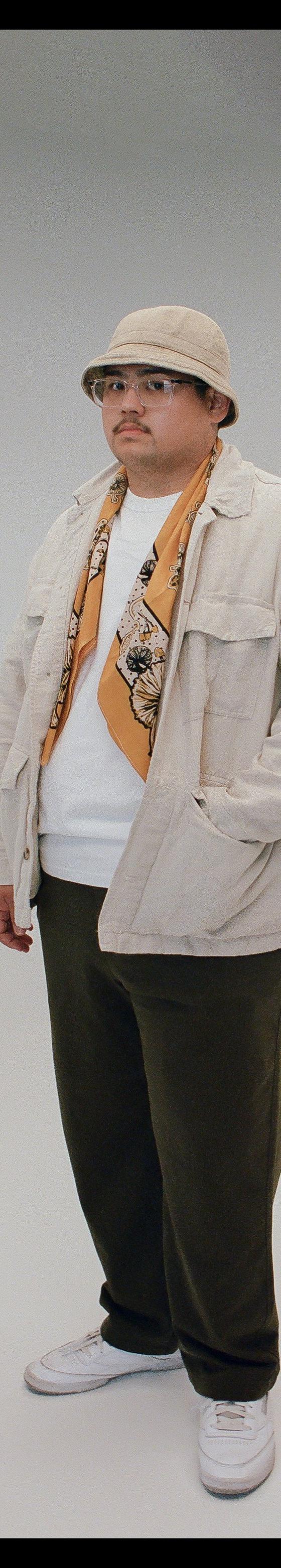 A man wearing a printed bandanna scarf with a cream overshirt and bucket hat
