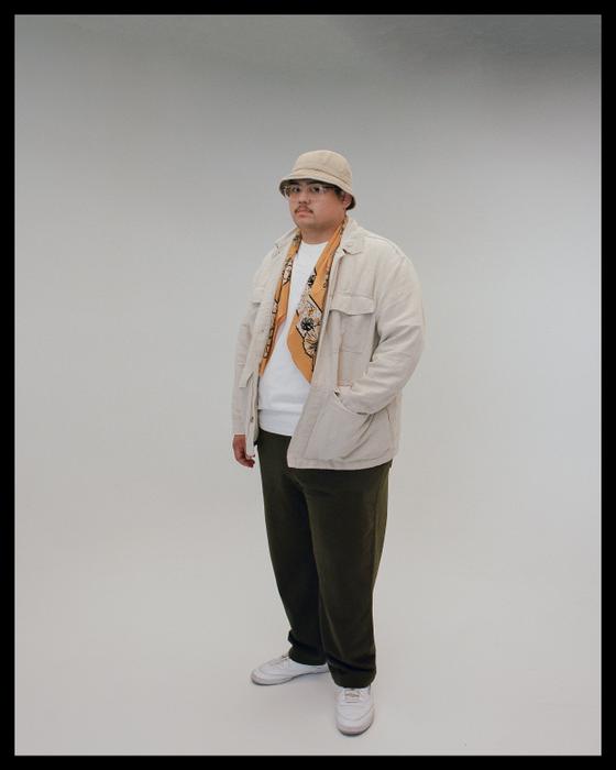 A man wearing a printed bandanna scarf with a cream overshirt and bucket hat
