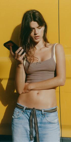 Organic Basics model in a ribbed brown bra top against a yellow wall