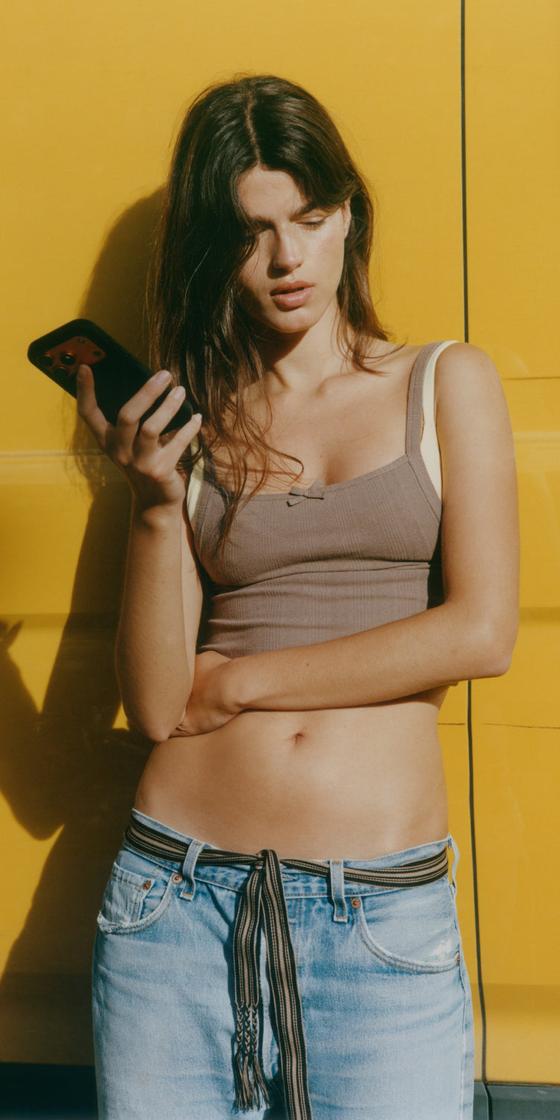 Organic Basics model in a ribbed brown bra top against a yellow wall