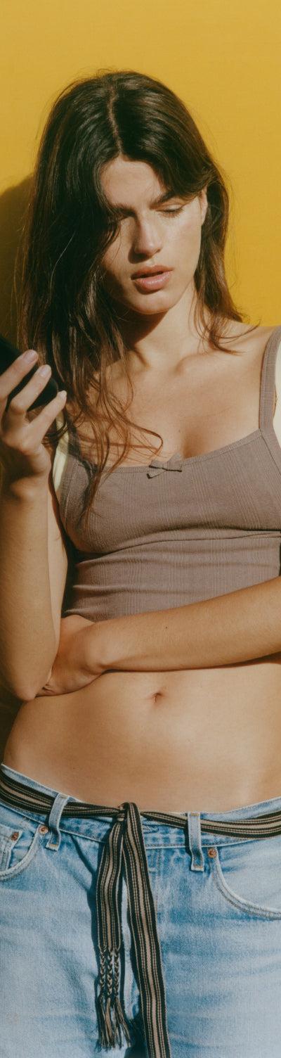 Organic Basics model in a ribbed brown bra top against a yellow wall