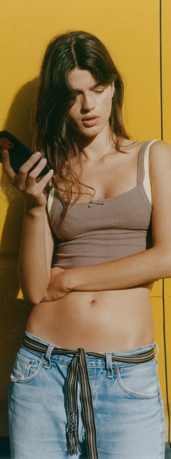 Organic Basics model in a ribbed brown bra top against a yellow wall
