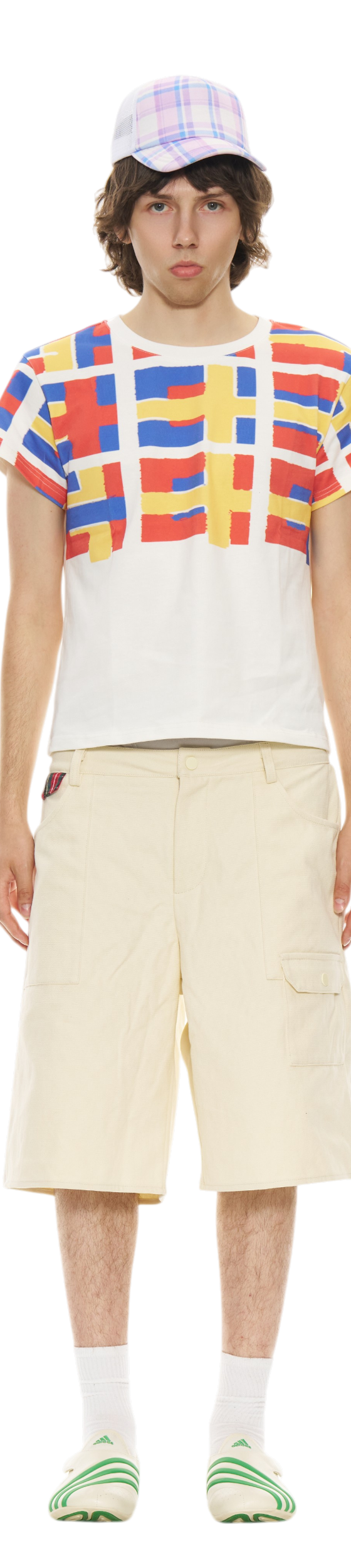 A man wearing a red, blue and yellow grid-print Organic Garmentz T-shirt with cream cargo shorts and a plaid cap