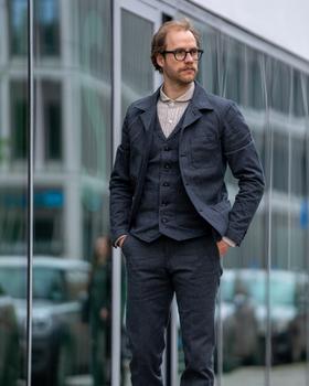 A man wearing a charcoal Orgueil wool work jacket, waistcoat and matching trousers over a striped shirt