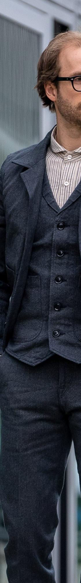 A man wearing a charcoal Orgueil wool work jacket, waistcoat and matching trousers over a striped shirt