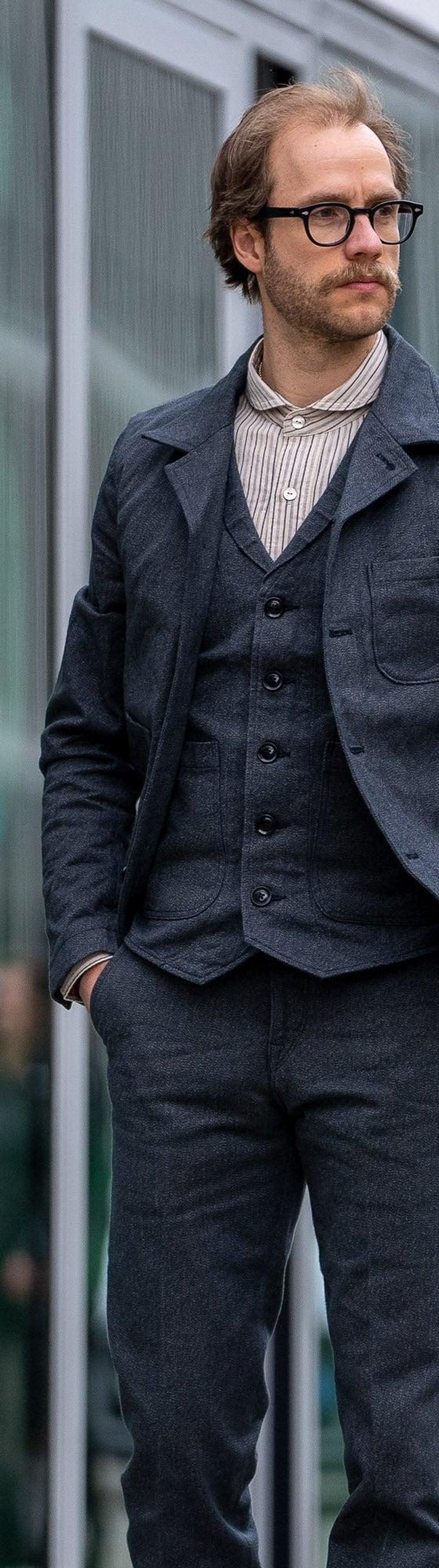 A man wearing a charcoal Orgueil wool work jacket, waistcoat and matching trousers over a striped shirt
