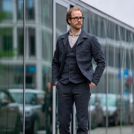 A man wearing a charcoal Orgueil wool work jacket, waistcoat and matching trousers over a striped shirt