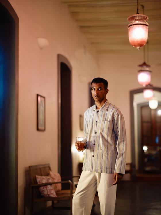 A man wearing a blue striped Original Madras Trading Company shirt jacket in a pink colonial hallway