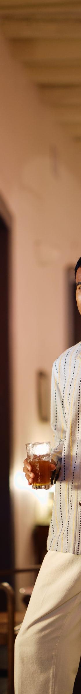 A man wearing a blue striped Original Madras Trading Company shirt jacket in a pink colonial hallway