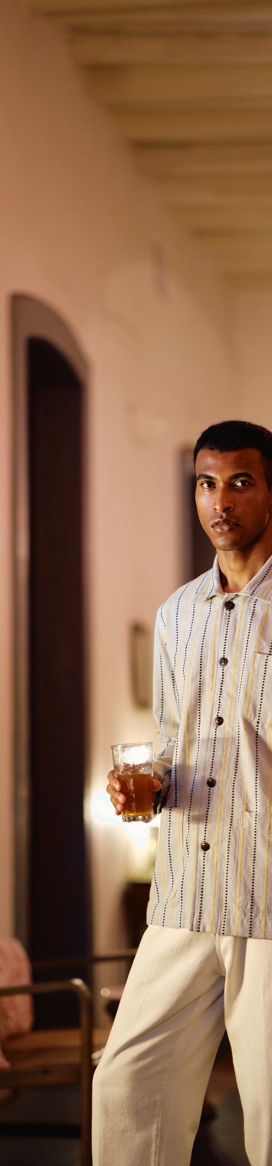A man wearing a blue striped Original Madras Trading Company shirt jacket in a pink colonial hallway