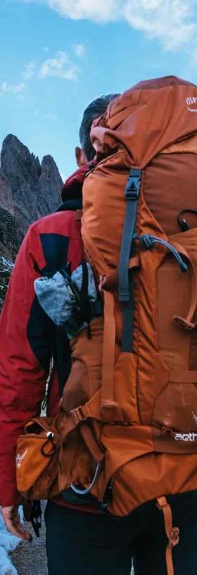 A hiker wearing a burnt-orange Osprey Aether 60 backpack on a snowy mountain ridge