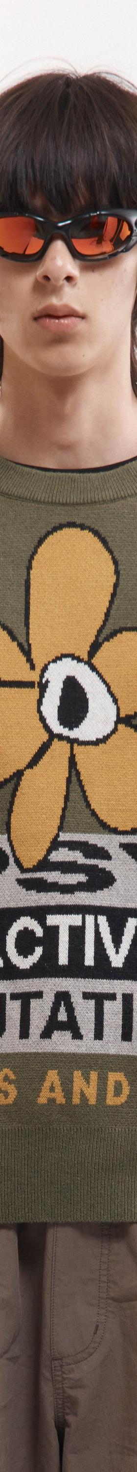 A man wearing an olive P.A.M. Perks and Mini intarsia knit sweater with a psychedelic flower motif