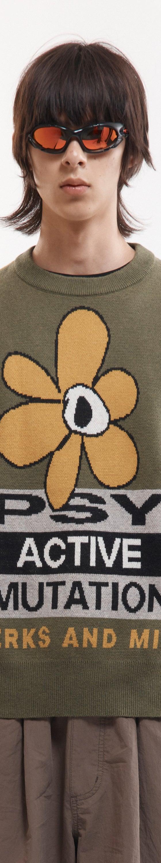 A man wearing an olive P.A.M. Perks and Mini intarsia knit sweater with a psychedelic flower motif