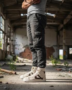 A man wearing grey cargo trousers and white Panam high-top sneakers in an empty warehouse