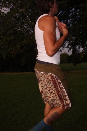 A man wearing a white tank top and olive paria /FARZANEH shorts with Ghalamkar print panels