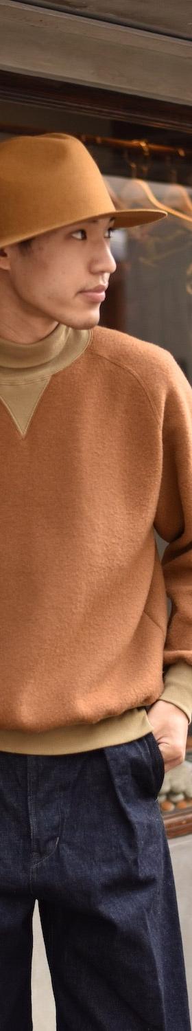 A man wearing a camel loopwheel Pherrow's sweatshirt with a felt hat and indigo denim trousers