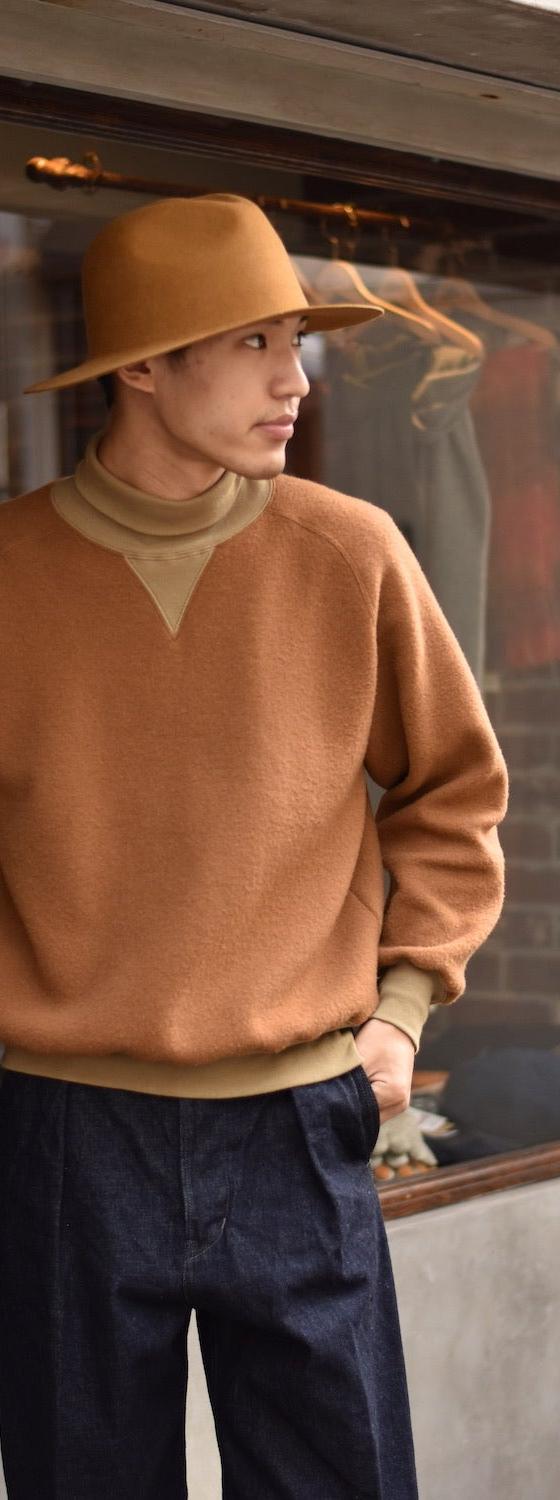 A man wearing a camel loopwheel Pherrow's sweatshirt with a felt hat and indigo denim trousers