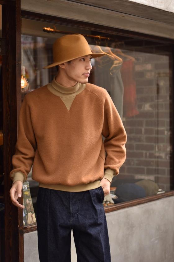 A man wearing a camel loopwheel Pherrow's sweatshirt with a felt hat and indigo denim trousers