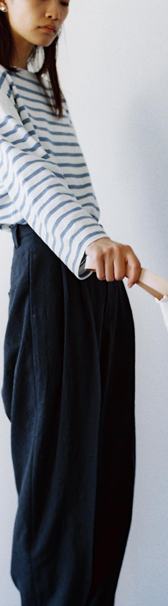 A woman wearing a blue and white striped Phlannèl top with dark wide-leg trousers, holding a white drawstring bag