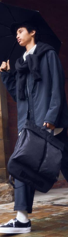 A man in a navy hooded coat carrying a black PORTER-YOSHIDA & CO. nylon tote bag
