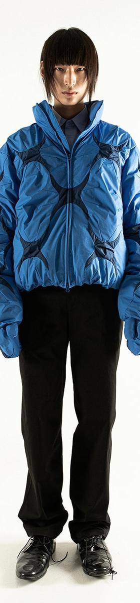 A model wearing a blue padded POST ARCHIVE FACTION bomber jacket with black trousers