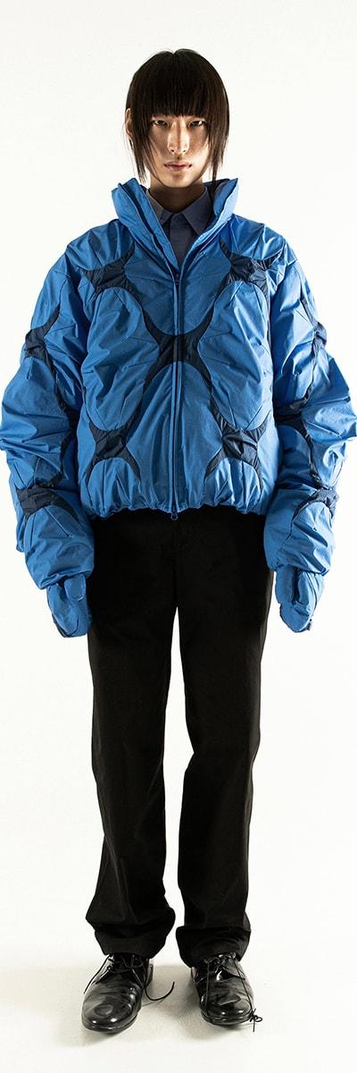 A model wearing a blue padded POST ARCHIVE FACTION bomber jacket with black trousers
