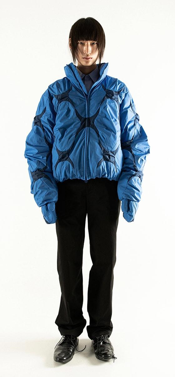 A model wearing a blue padded POST ARCHIVE FACTION bomber jacket with black trousers