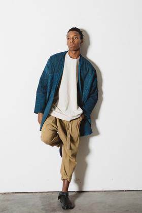 A man wearing an indigo quilted Prospective Flow haori jacket over a cream tee and tan cropped trousers