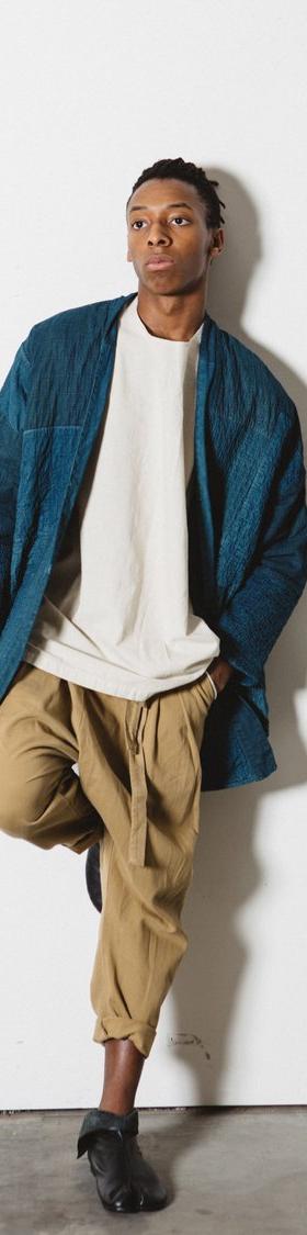 A man wearing an indigo quilted Prospective Flow haori jacket over a cream tee and tan cropped trousers