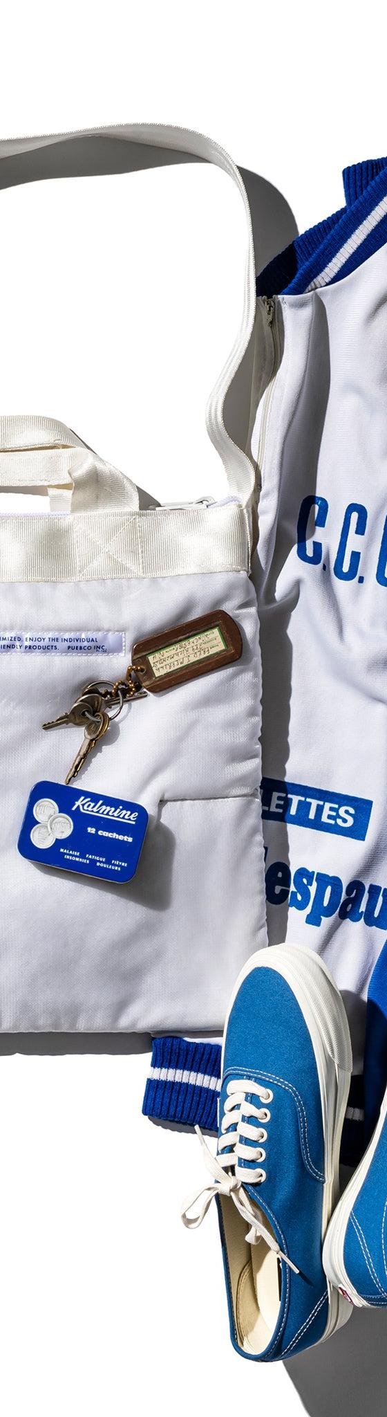 A white quilted Puebco tote bag styled with a blue track jacket and sneakers