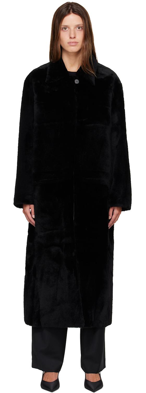 A woman wearing a long black R2W shearling coat with black trousers