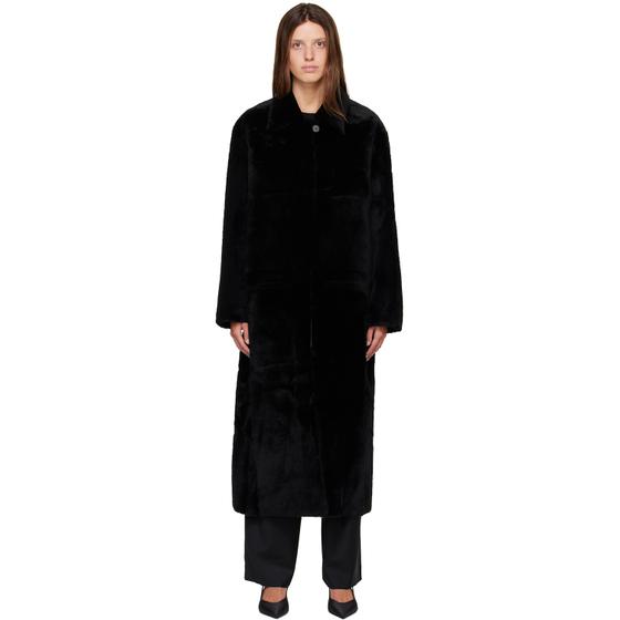 A woman wearing a long black R2W shearling coat with black trousers
