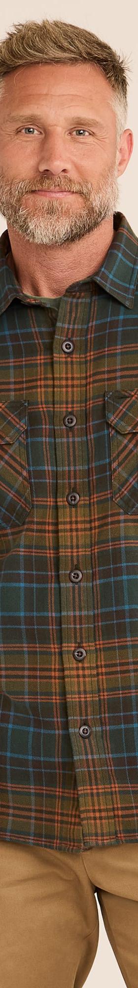 A man wearing a green and orange plaid Railcar Fine Goods flannel work shirt with tan trousers