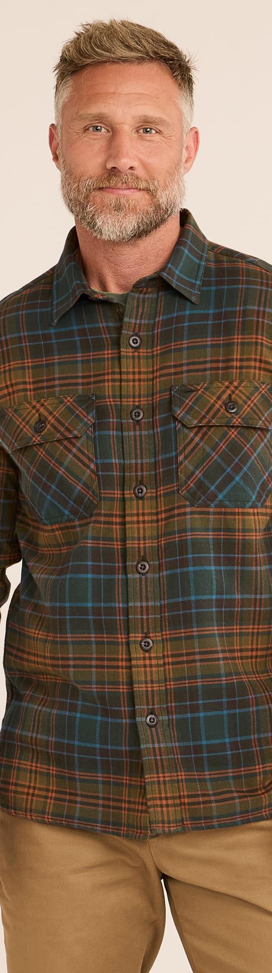 A man wearing a green and orange plaid Railcar Fine Goods flannel work shirt with tan trousers