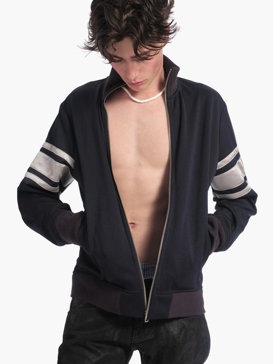 A man wearing a navy Raimundo Langlois striped-sleeve track jacket with black jeans