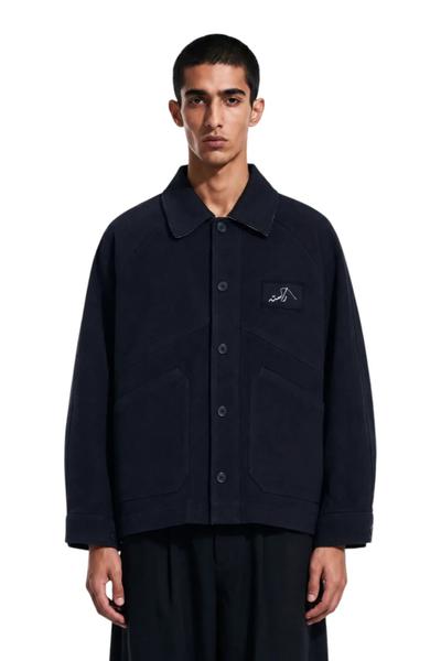 A man wearing a navy Rastah chore jacket with wide black trousers