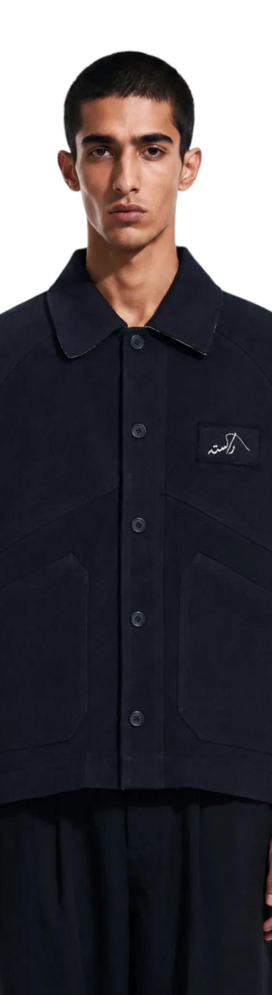 A man wearing a navy Rastah chore jacket with wide black trousers