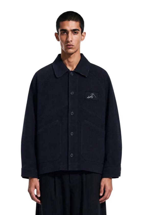 A man wearing a navy Rastah chore jacket with wide black trousers