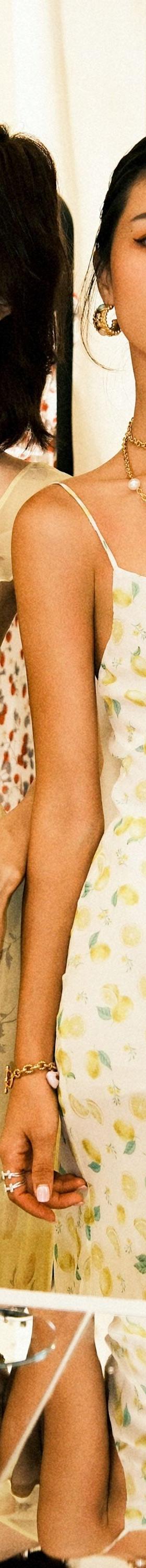 Two women wearing pastel yellow floral and lemon-print Realisation Par slip dresses in a boutique