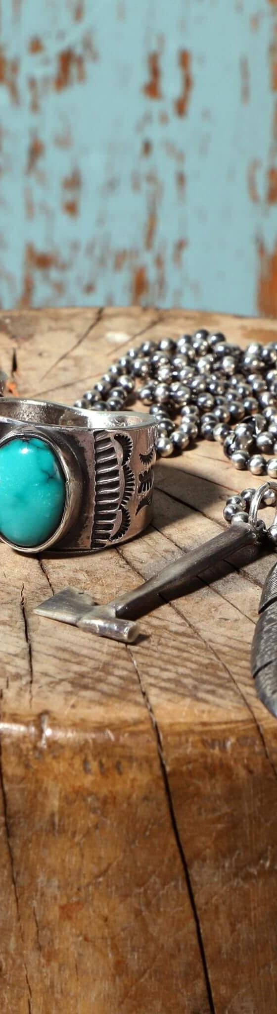 Hand-stamped sterling silver rings with turquoise stones and a feather pendant necklace arranged on a weathered wood stump
