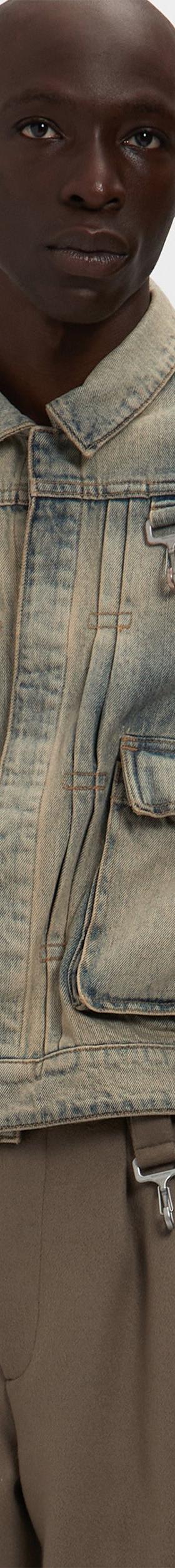 A man wearing a washed denim Reese Cooper utility jacket with cargo pockets over brown trousers