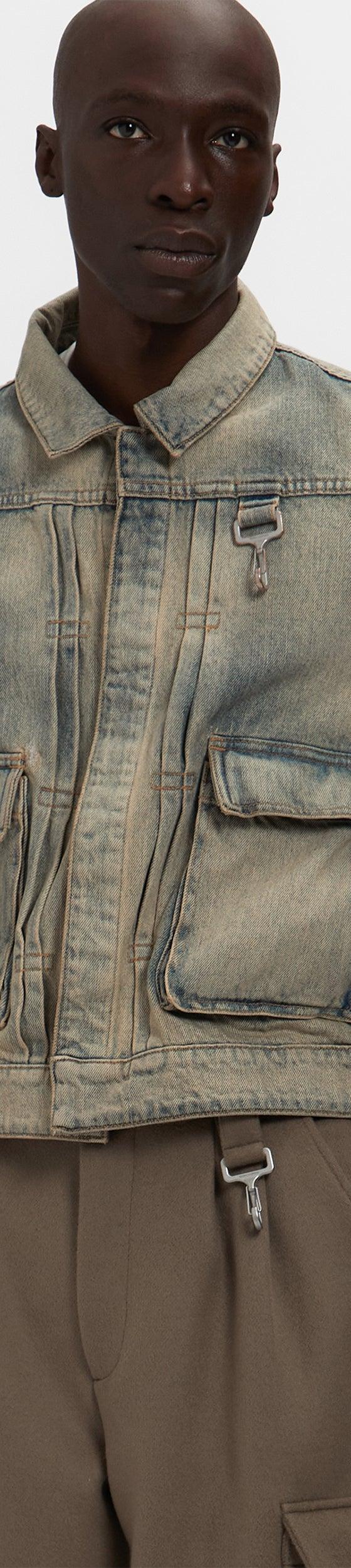 A man wearing a washed denim Reese Cooper utility jacket with cargo pockets over brown trousers
