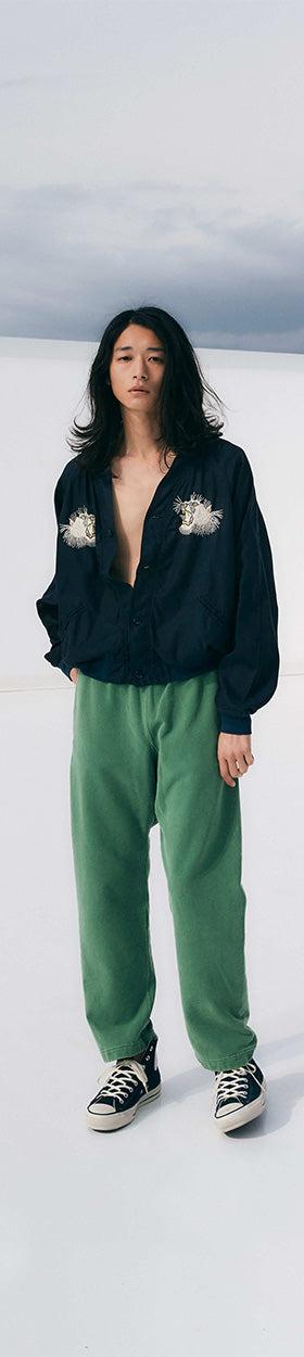 A woman wearing a navy REMI RELIEF pullover shirt with green sweatpants