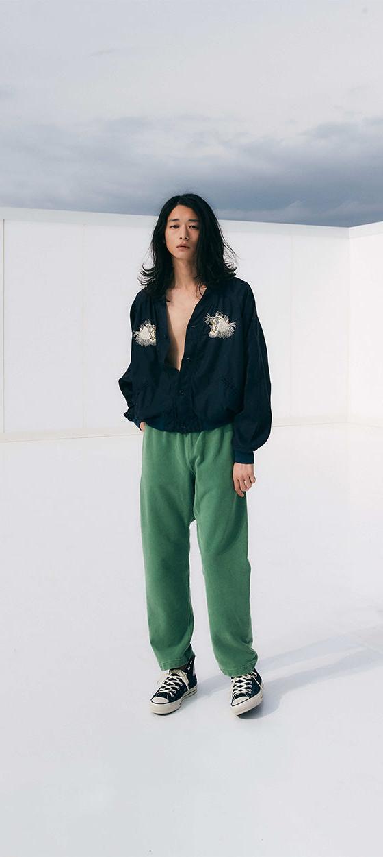 A woman wearing a navy REMI RELIEF pullover shirt with green sweatpants
