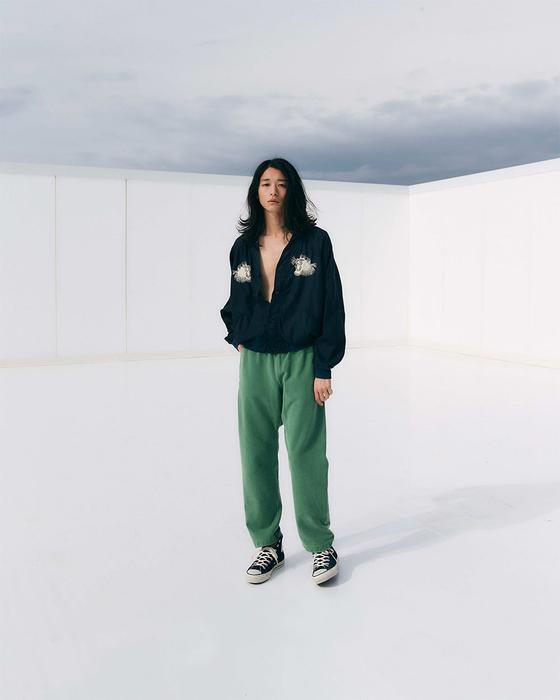 A woman wearing a navy REMI RELIEF pullover shirt with green sweatpants