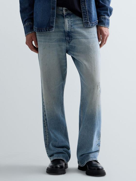 A man wearing light-wash Replay straight-leg jeans with a denim jacket