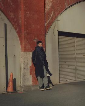 A man wearing a navy Reproduction of Found coat and grey trousers with black military trainers on a Tokyo street