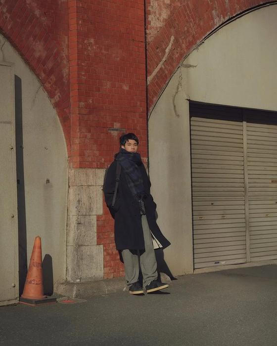 A man wearing a navy Reproduction of Found coat and grey trousers with black military trainers on a Tokyo street