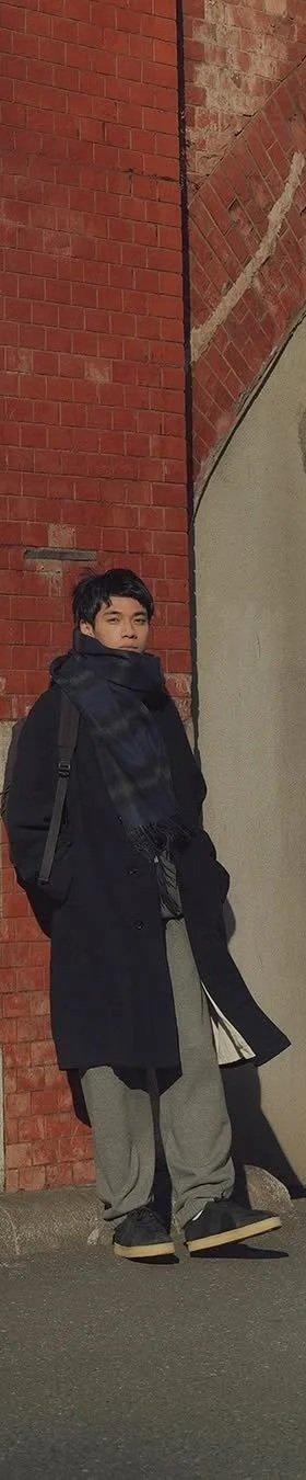 A man wearing a navy Reproduction of Found coat and grey trousers with black military trainers on a Tokyo street