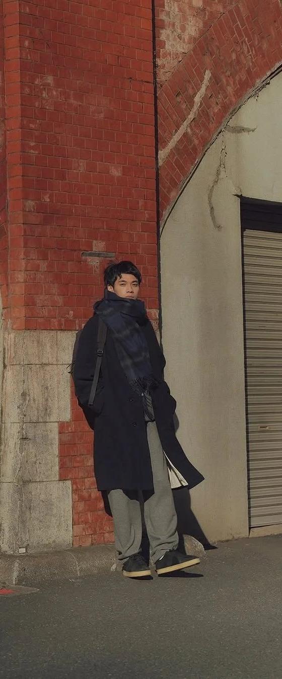 A man wearing a navy Reproduction of Found coat and grey trousers with black military trainers on a Tokyo street